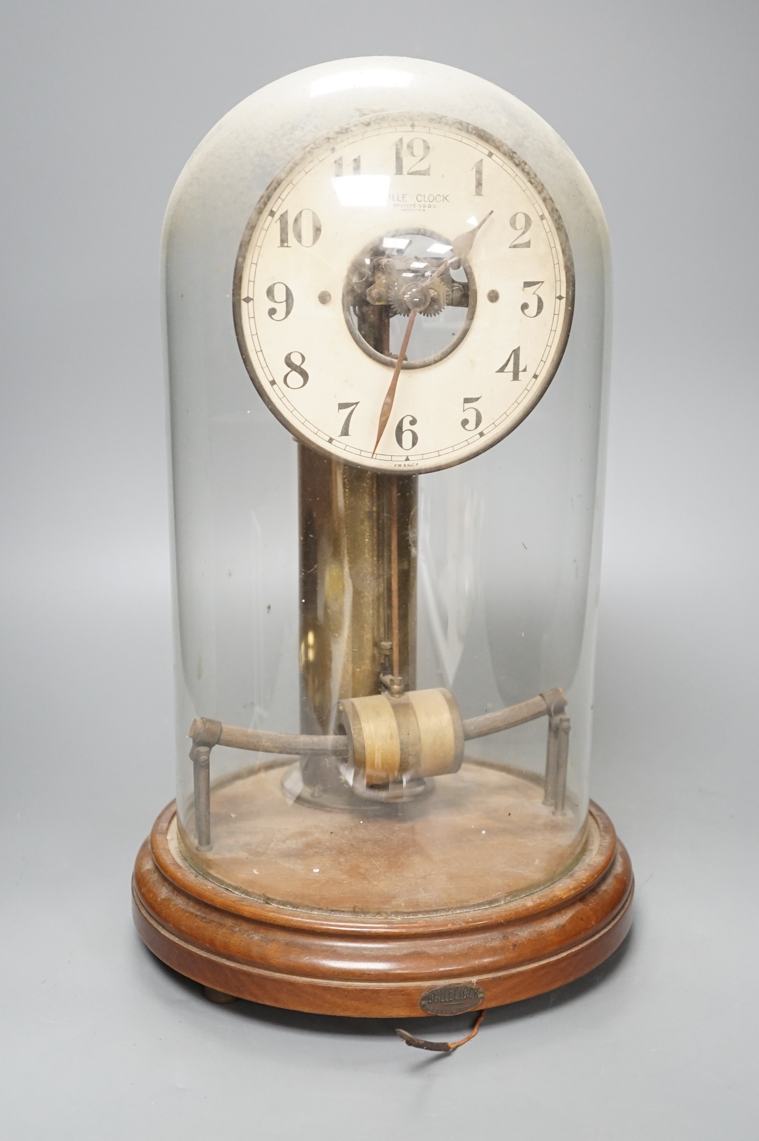 A Bulle electric pendulum clock, with large central brass pillar supporting the 14cm. dial, under a glass dome on a mahogany plinth
